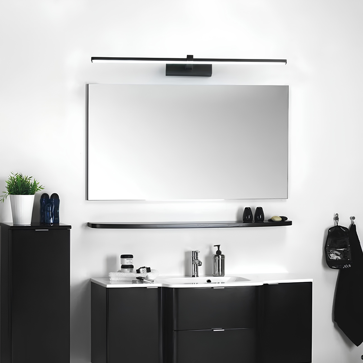 Matte black LED vanity bar light illuminating a full-width mirror above a floating black timber shelf and vanity in a monochrome bathroom.
