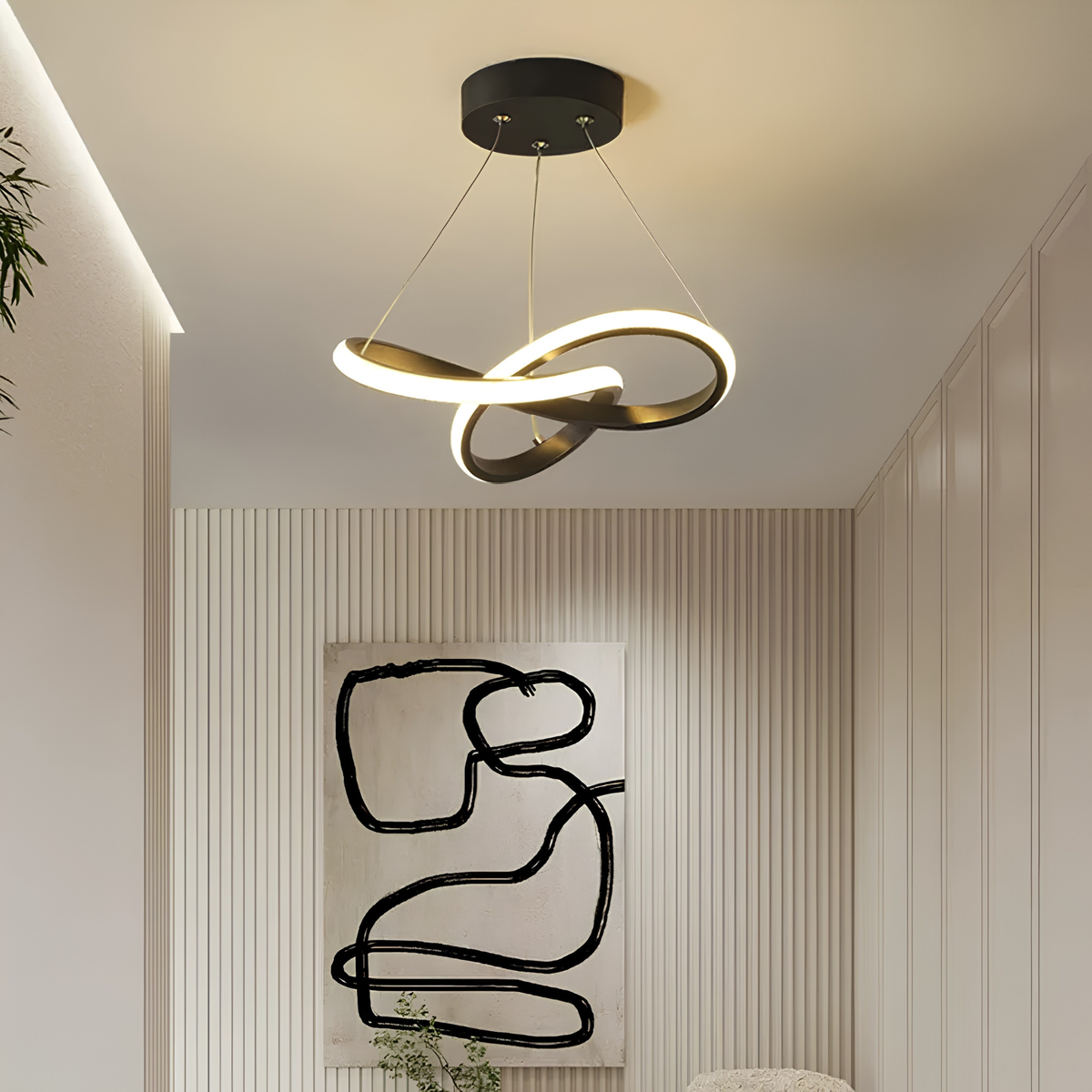 Matte black sculptural interlocking-ring LED pendant light glowing warmly in an entry corridor beside abstract wall art and an indoor plant.