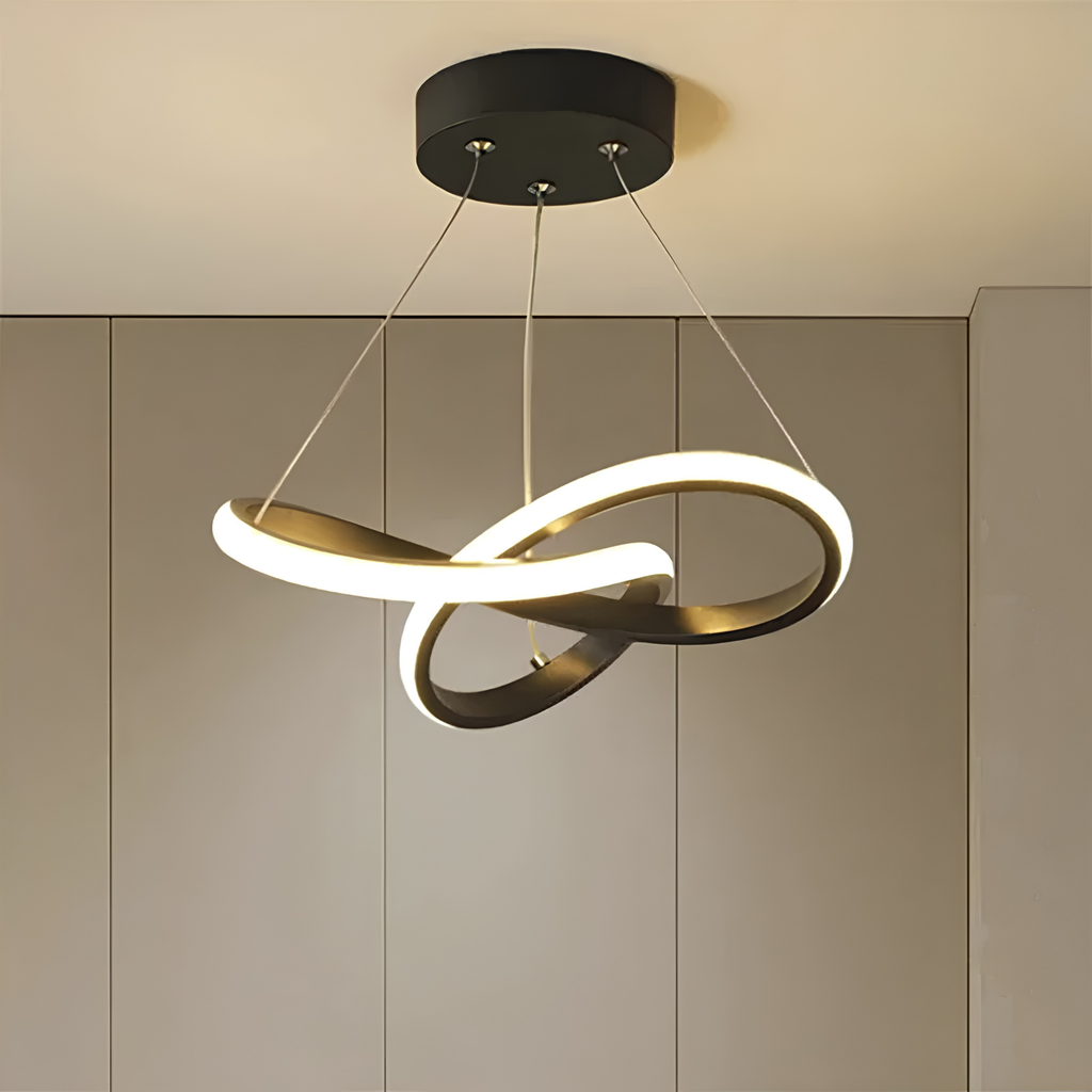 Matte black sculptural interlocking-ring LED pendant light illuminated against ribbed wall panelling in a warm-toned interior.