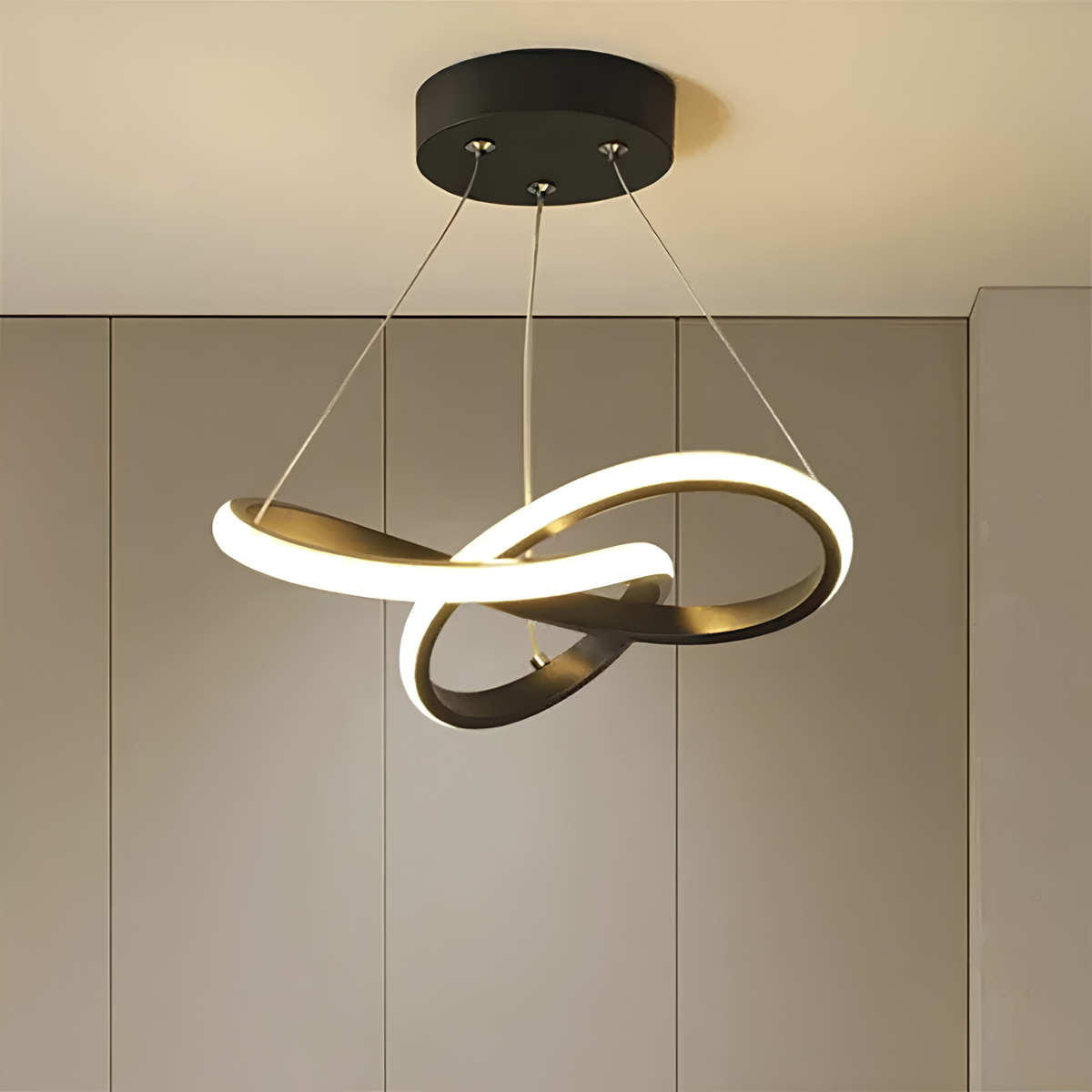 Matte black sculptural interlocking-ring LED pendant light illuminated against ribbed wall panelling in a warm-toned interior.