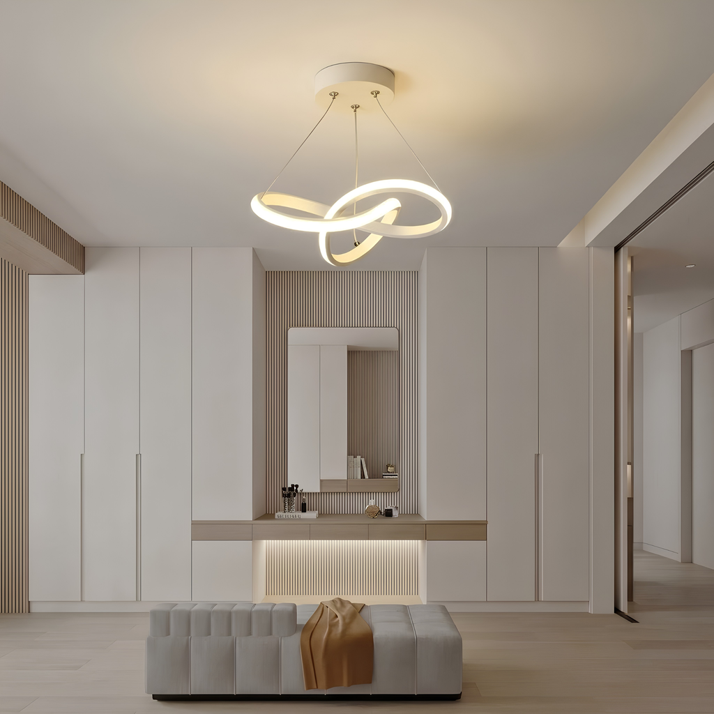 White sculptural interlocking-ring LED pendant light illuminated above a dressing table in a cloakroom, with a supplier caption overlay.