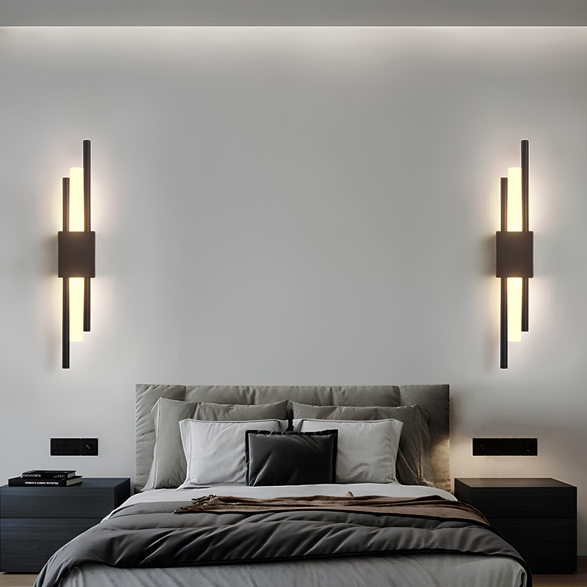 Pair of matte black cylindrical up-down wall sconces flanking a bed in a minimalist charcoal-toned bedroom.