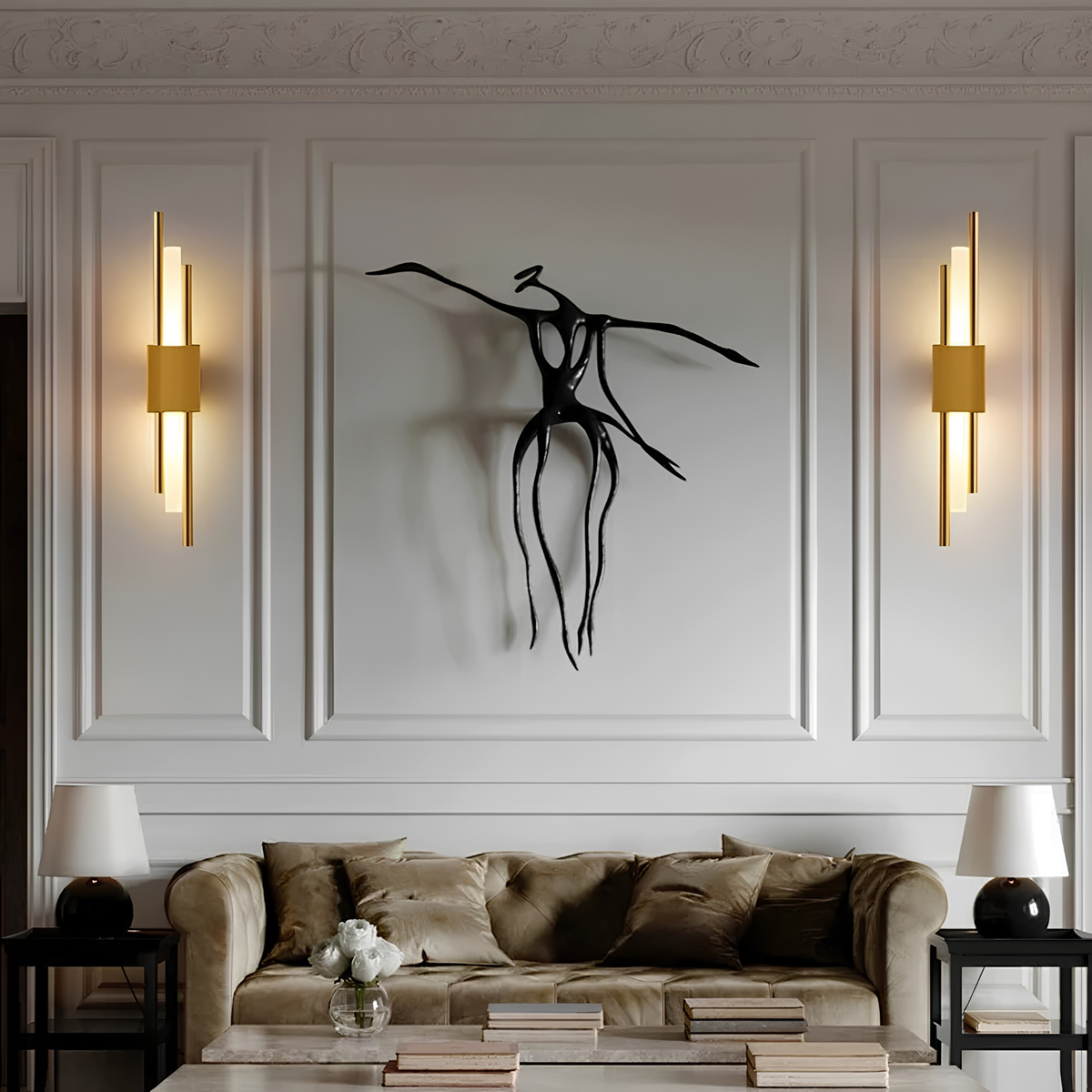 Pair of brushed brass cylindrical up-down wall sconces flanking a sculptural bronze wall artwork in an elegant panelled living room.
