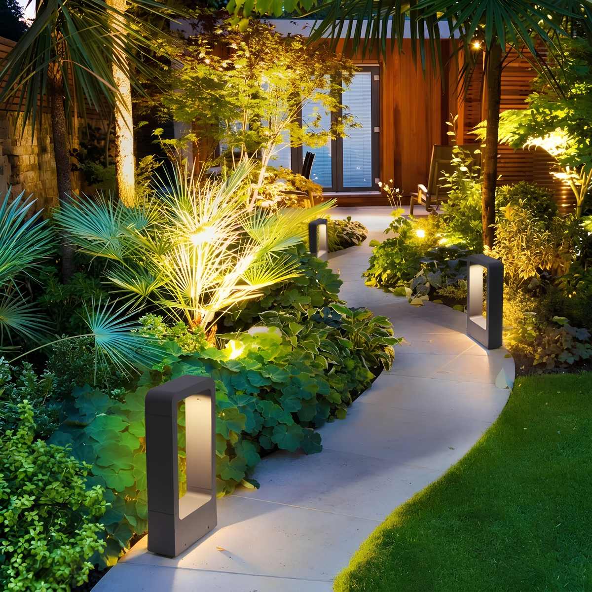 Row of matte black LED pathway bollard lights illuminating a curved garden path through tropical planting to a timber-clad home at night.