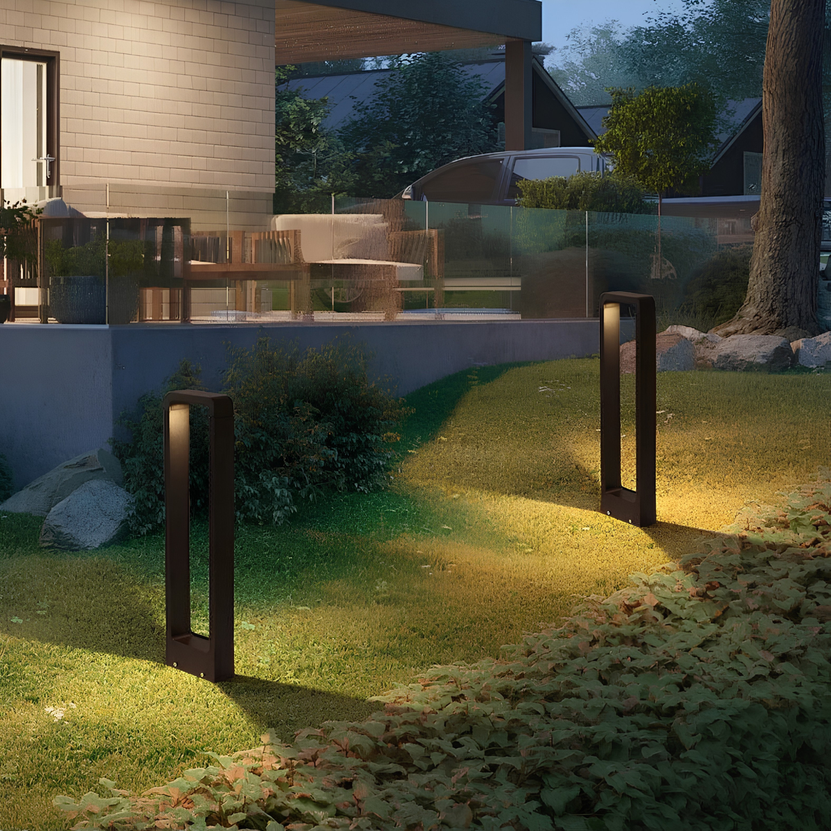 Matte black LED pathway bollard lights illuminating a landscaped garden beside a glass balustrade and driveway at a modern home.